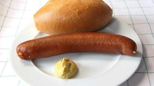 Frankfurter Rindswurst mit Senf und Brötchen auf einem Teller