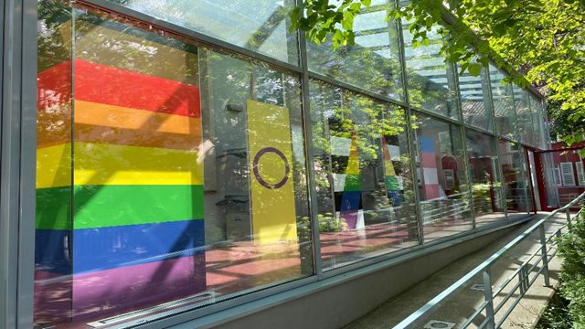 Durch die großen Fenster des Bibelhauses sind Regenbogenflaggen zu sehen.