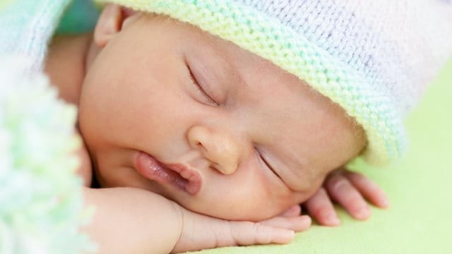 Schlafendes Baby mit Strickmütze vor grünem Hintergrund