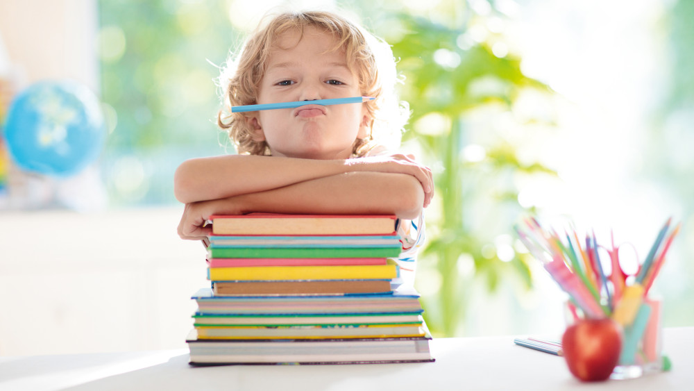 Schulkind mit einem Stapel Bücher und Stiften