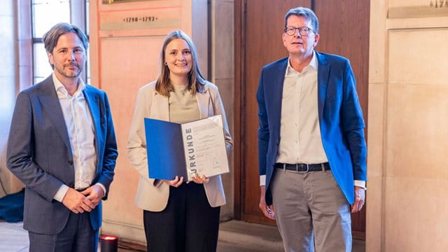 Sophie Sommer erhält die Urkunde für den Wächterpreis 2025 Sophie Sommer steht in der Mitte von Stadtrat Marcus Gwechenberger und Moritz Döbler und hält die Urkunde für den Wächterpreis 2025, Foto: Martin Leissl