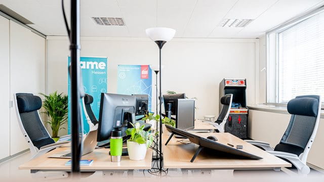 Die neuen Räumlichkeiten sind speziell für die Bedürfnisse von Game-Entwicklern eingerichtet. Blick in ein Büroraum mit Bildschirmen, Bürostühlen und einem Spielautomat, Foto: Michael Braunschädel