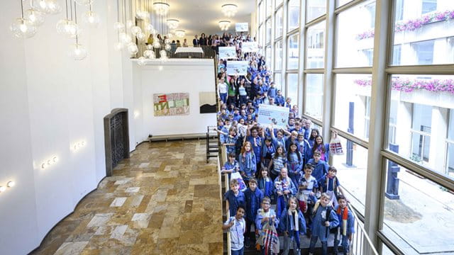 Nachhaltigkeitspreis 2025 alle Siegerschulen Schulkinder stehen auf der Treppe des Römerfoyers und halten fünf Schilder mit dem Namen der jeweiligen Schule in die Höhe, Foto: Salome Roessler