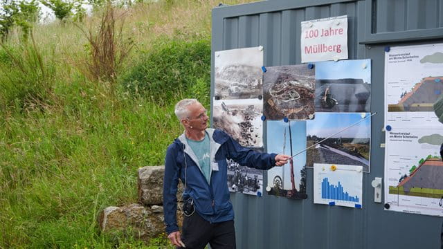 Andreas Müller informiert über die Geschichte und Entwicklung des Monte Scherbelino Ein Mann steht vor einer Containerwand am Monte Scherbelino und zeigt mit einem Zeigestock auf ausgedruckte Grafiken, Foto: Stefan Cop