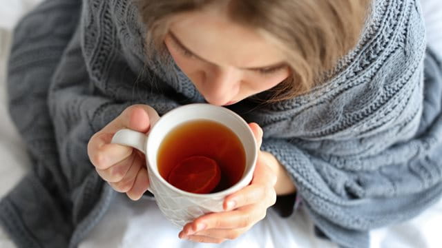 Young ill woman with cup of hot tea at home, closeup