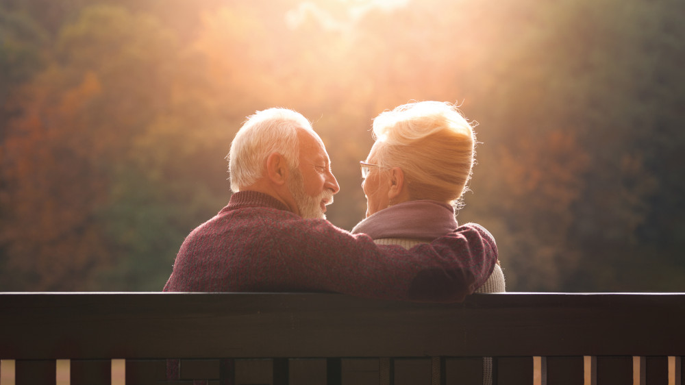 Senior couple sitting on bench in autumn park and looking sunset