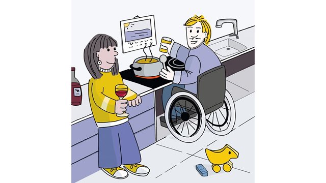 In der Küche steht eine Frau mit Weinglas in der Hand. Hinter ihr ist ein Mann beim Kochen. Seinen Rollstuhl hat er halb unter den barrierefreien Herd gefahren.