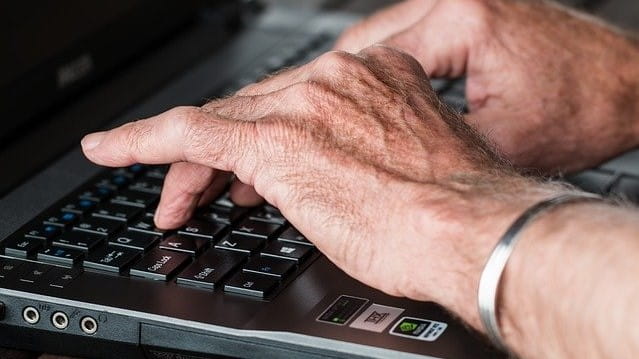 Hände eines älteren Mannes an einer Laptop-Tastatur. 