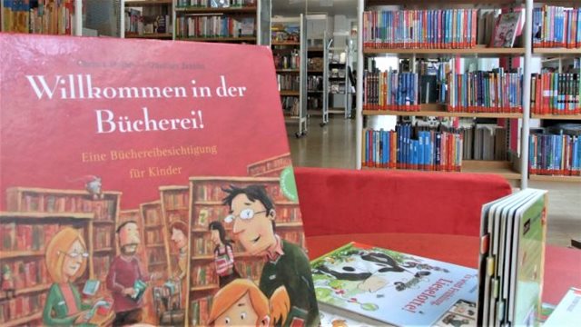 Das Kinderbuch "Willkommen in der Bücherei" ist auf einem Tisch aufgestellt. 