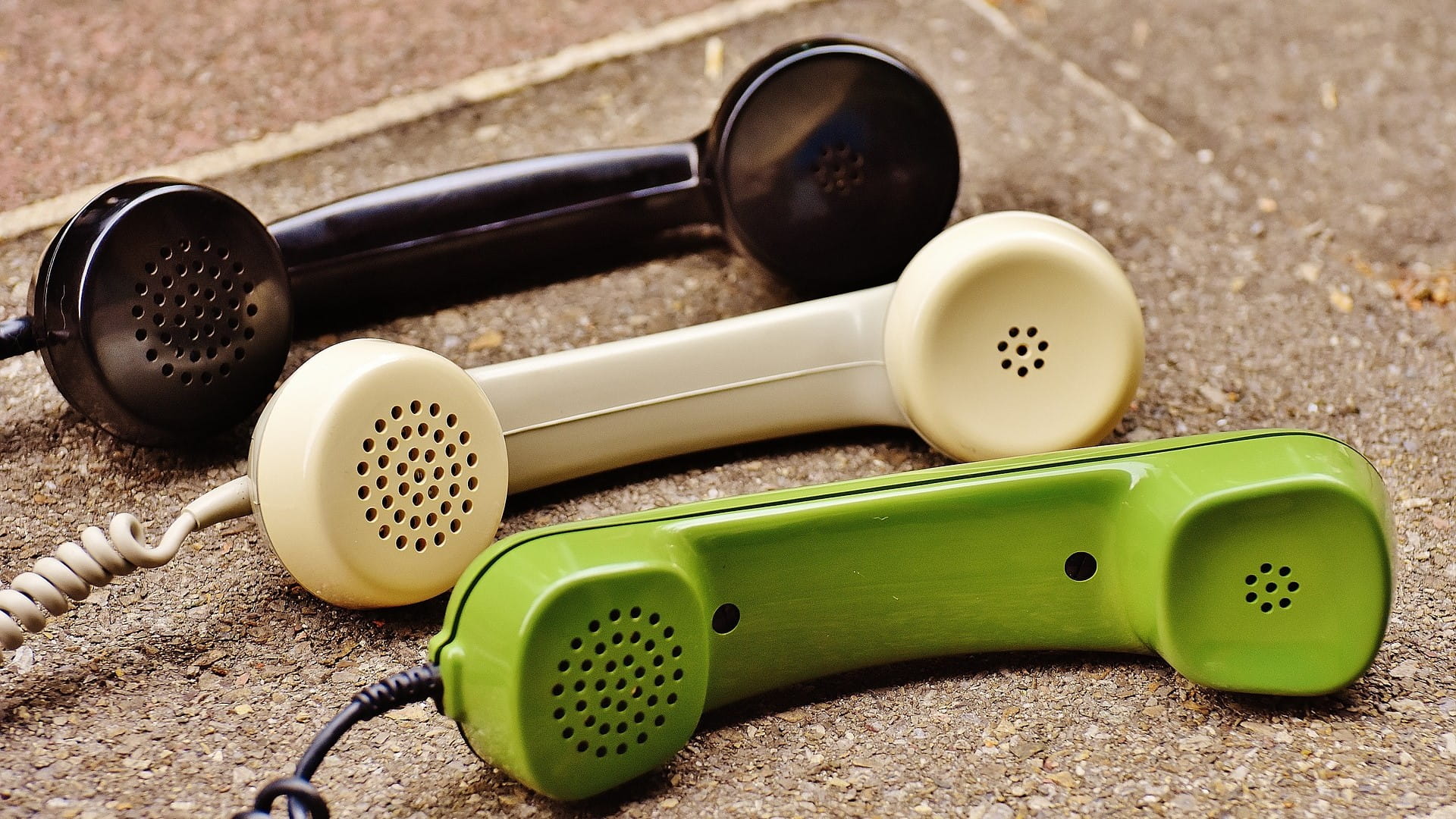Drei almodische Telefonhörer in grün, schwarz und weiß.