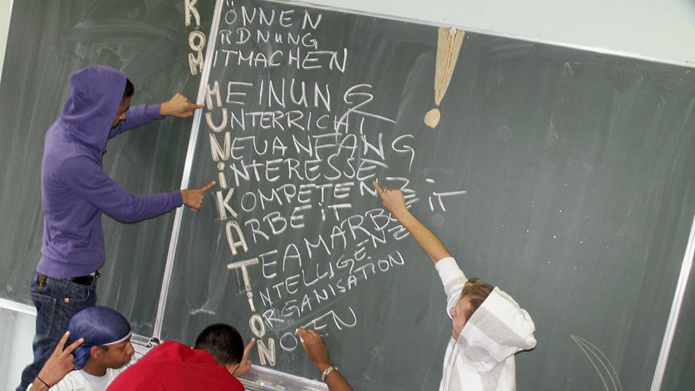 Schüler schreiben mit weißer Kreide das Wort Kommunikation an eine Tafel.