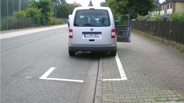 Ein Fahrzeug parkt halb auf dem Gehweg innerhalb einer Parkflächenmarkierung 