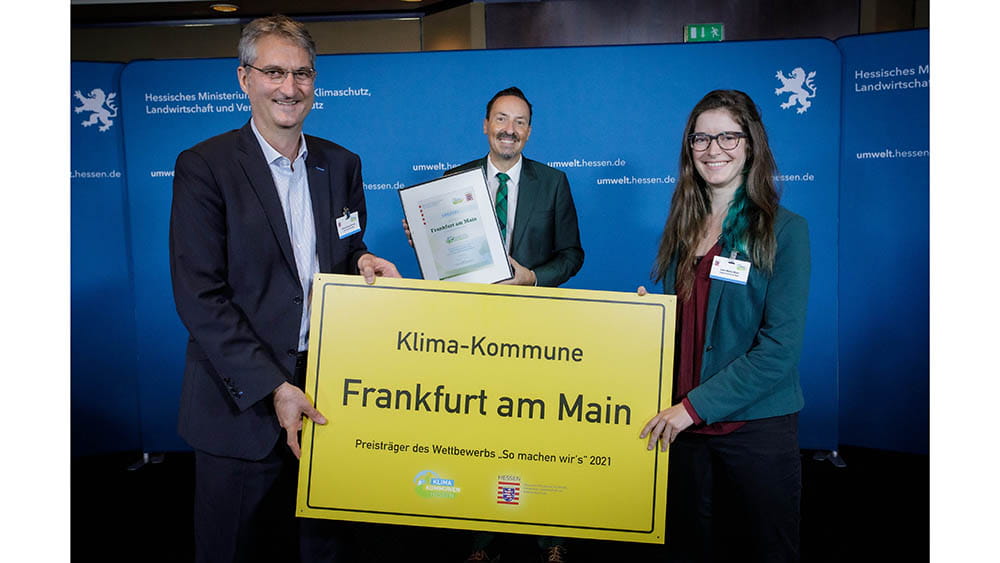 Hans-Georg Dannert (links) und Lara Mohr (rechts) nahmen das symbolische Ortsschild als Gewinnerkommune von Staatssekretär Oliver Conz vom HMUKLV entgegen