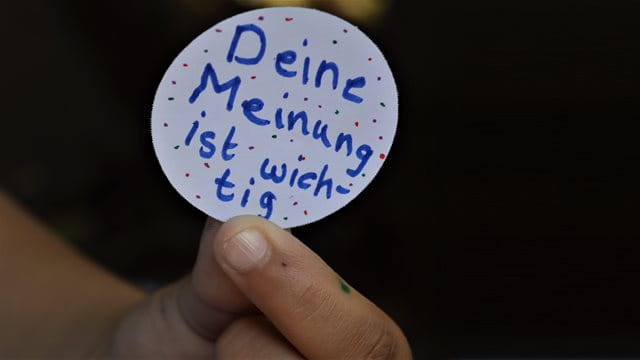 A child holds a button with the inscription "Your opinion is important" into the camera; Photo: Daniela Krenzer