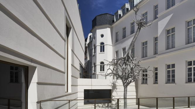 Ariel Schlesingers Skultpur "Untitled" 2019 besteht aus zwei ineinander verkeilten Stahl-Bäumen. Die eine Krone hält die andere Krone, während die Wurzeln gen Himmel zeigen, im Hintergund links die Fassade des Anbaus des  Jüdischen Museums, rechts die Fassade des sanierten Altbaus.