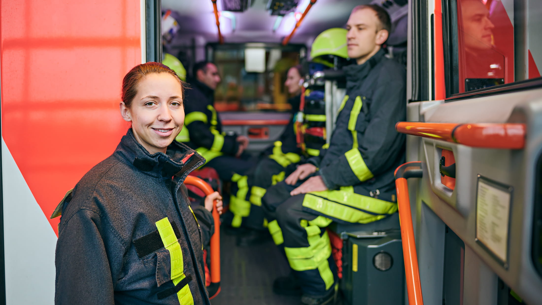 Eine Feuerwehrfrau steigt zu ihren Kollegen in das Feuerwehrfahrzeug.