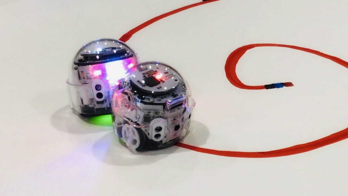 Zwei Ozobot Roboter fahren auf roter Linie