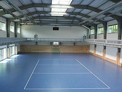 Innenansicht der modernen Sporthalle mit blauem Kunststoffboden und zahlreichen Fenstern