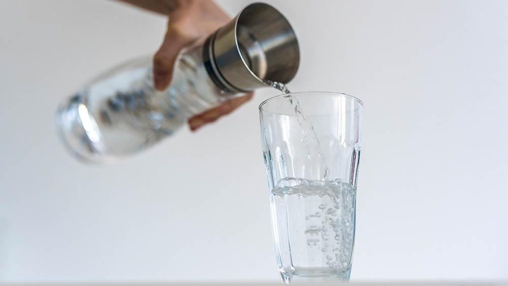Trinkwasser wird aus einer Karaffe in ein Glas eingeschenkt