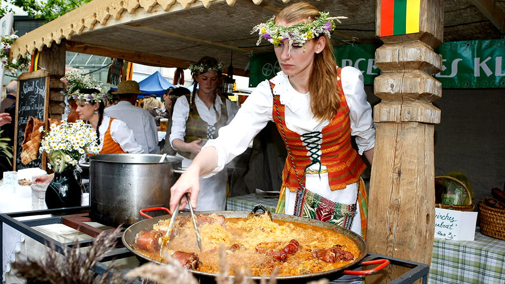 Eine Frau in Tracht bei der Zubereitung von Gerichten auf dem Schweizer Straßenfest, Foto: Aktionsgemeinschaft Schweizerstraße e.V.